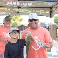 Gabe Edney presenting a $100 bill to a child fisher at the 2023 Kids' Fishing Derby, with Jimmy Clark from Today in Ag in the background.
