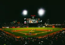 Action shot of an MLB game at night with players in motion and fans cheering in the stadium.