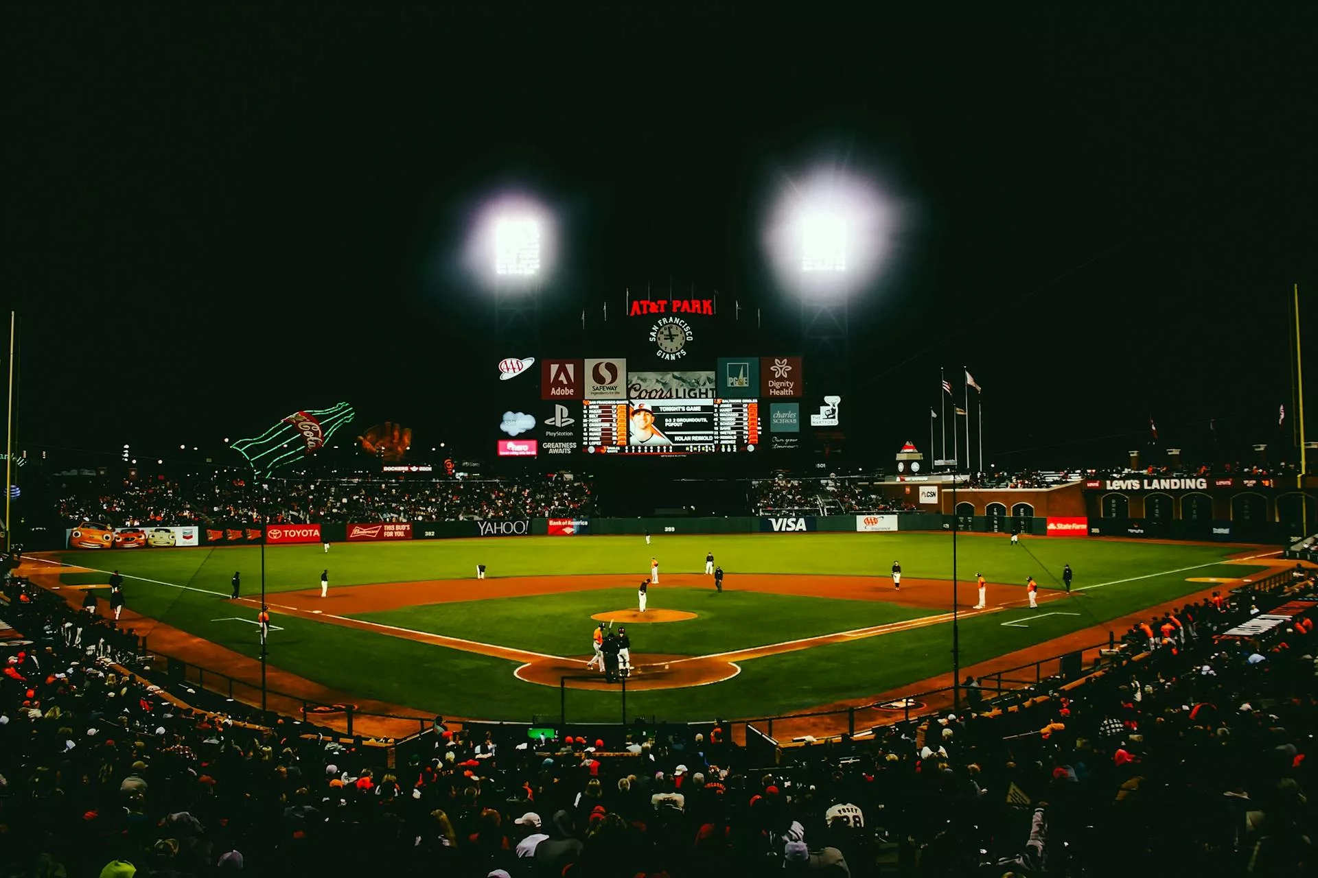 Action shot of an MLB game at night with players in motion and fans cheering in the stadium.