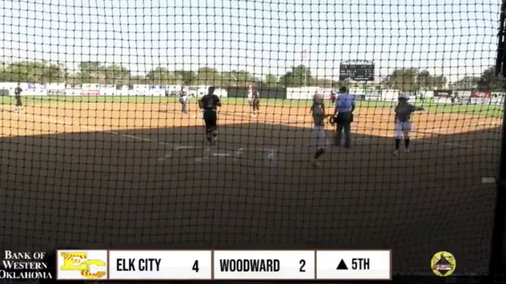 Softball game between Elk City and Woodward, with Elk City about to lead 5-2 after scoring a run in the 5th inning. Players are seen returning to their positions as the scoreboard still shows 4-2.