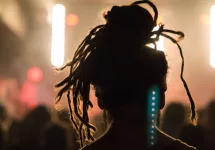 Close up portrait of an anonymous performer/ silhouette with dreadlocks^ back to camera^ watching a concert on stage with music^ retro light effect^ flashlight and spotlight in a festival.