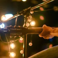 Rear view of the man sitting play acoustic guitar on the outdoor concert with a microphone stand in the front^ musical concept.