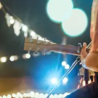Musical and enjoyment concepts. Rear view of the man sitting play acoustic guitar on the outdoor concert with a microphone stand in the front.