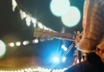 Musical and enjoyment concepts. Rear view of the man sitting play acoustic guitar on the outdoor concert with a microphone stand in the front.