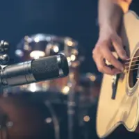 Male musician playing acoustic guitar behind microphone in recording studio.