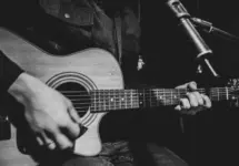The guitarist plays an acoustic guitar with a capo in front of a microphone. The concept of music recording^ rehearsal or live performance.