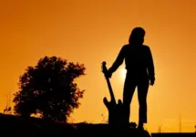 Silhouette Hipster woman with guitars in the meadow.