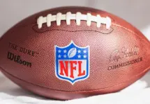 NFL Wilson Duke ball over a white sofa in a home. Sun light comes from a window.