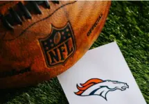 Denver Broncos NFL team Logo and American football ball on Green Grass.