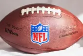 NFL Wilson Duke ball over a white sofa in a home. Sun light comes from a window.