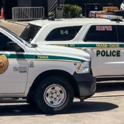 Two Miami-Dade police K-9 cars are parked near a metal security fence on a bright sunny day. Miami^ Florida^ USA^ June 16th 2025