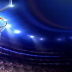 Basketball arena view of basketball hoop in dimmed arena^ crowd in silhouette^ lights turned on brightly
