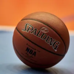 Close-up of a Spalding NBA basketball resting on a blue and orange court^ focusing on the texture of the ball and the surrounding vibrant colors of the court.