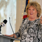 Carol Hadan points to Doug Gibb sitting in the crowd as she accepts and offers remarks following receipt of the 2022 Thomas B. Herring Award during the Galesburg Area Chamber of Commerce’s Thanksgiving Luncheon on Monday afternoon at Cedar Creek Hall. (Photo by Bill Gaither)