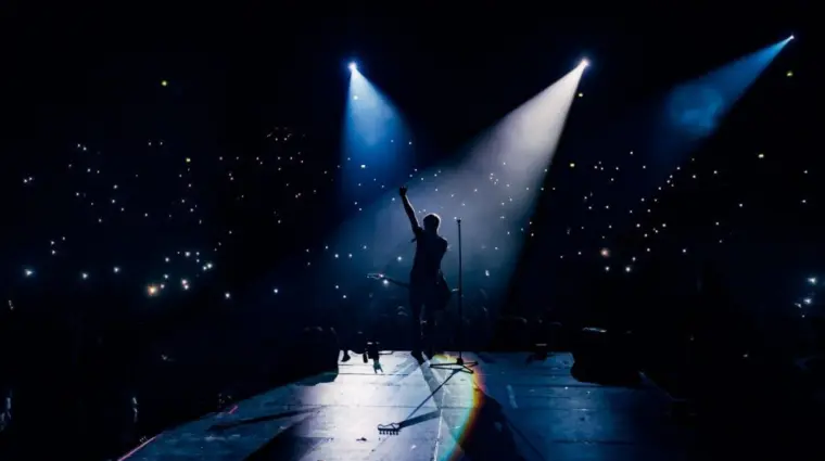 View from the stage stadium. Vocalist of a popular pop band on the background of the flashlights of phones during a concert. Fans switch on lights on smart phones on tribunes. Crowd waving cellphones