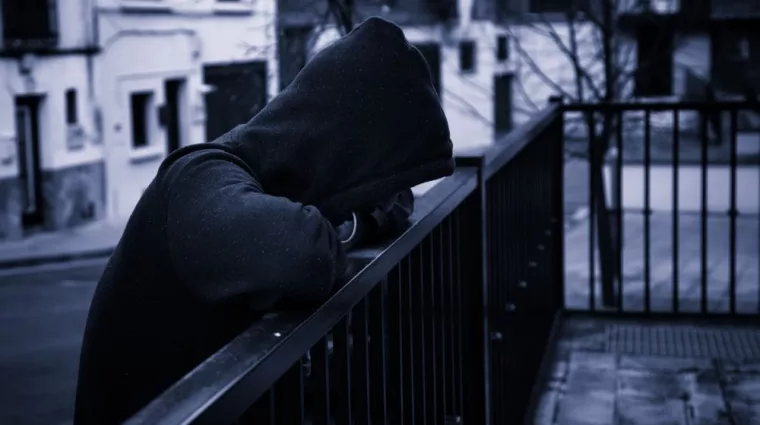 silhouette of man in dark hoodie outside leaning on fence