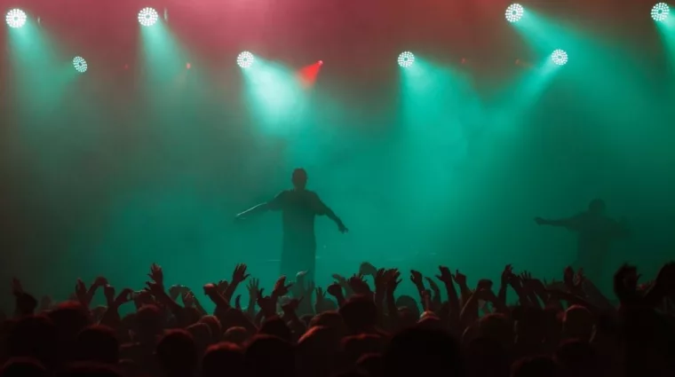 Rap singer performing on concert in music hall. Silhouette of rapper singing on stage in night club. Popuar hip hop music festival. Crowd of fans partying on dance floor