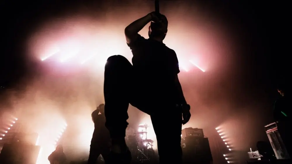 A dark silhouette of a singer on the stage. Good-looking background^ bright stag lights. A concert of a famous music band