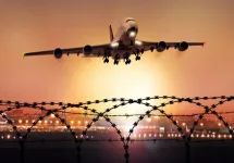 Passenger plane takes off at dusk^ in the background the lights of the airport can be seen and in the foreground a barbed wire fence