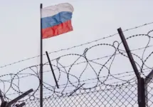 View of russian flag behind barbed wire against cloudy sky. Concept anti-Russian sanctions. A border post on the border of Russia.