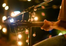 Rear view of the man sitting play acoustic guitar on the outdoor concert with a microphone stand in the front^ musical concept.