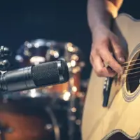 Male musician playing acoustic guitar behind microphone in recording studio.