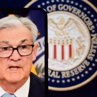 Federal Reserve (Fed) Chair Jerome Powell is visible on smartphone screen. In the background^ an inflation rate chart is displayed.