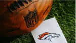 Denver Broncos NFL team Logo and American football ball on Green Grass.