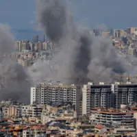 Multiple large plumes of thick grey smoke billow from residential apartment complexes following an explosion or missile strike in a crowded urban skyline. Jan 3 2021 in Iran