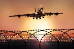 Passenger plane takes off at dusk^ in the background the lights of the airport can be seen and in the foreground a barbed wire fence