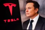 Elon Musk^ CEO of Tesla^ in a formal suit with the Tesla logo in the background. The image depicts electric vehicles^ innovations^ and tech leadership.