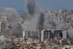 Multiple large plumes of thick grey smoke billow from residential apartment complexes following an explosion or missile strike in a crowded urban skyline. Jan 3 2021 in Iran