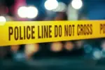 Yellow Tape Showing Text "Police Line Do Not Cross" Restricting a Crime Scene Area At Night. Close Up Aesthetic Shot with Bokeh Effect and Flickering Lights. Criminal on the Loose Strikes Again