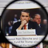Close up through magnifying lens capturing legal professional Todd Blanche with nameplate at desk during hearing. Law and courtroom justice journalism concept.