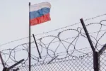 View of russian flag behind barbed wire against cloudy sky. Concept anti-Russian sanctions. A border post on the border of Russia.