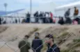 Barbed wire in refugee camp. Migrants behind chain link fence in camp. Group of people behind fence. Concept of prison^ freedom^ barrier^ security and migration. Refugees on their way to EU.