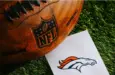 Denver Broncos NFL team Logo and American football ball on Green Grass.