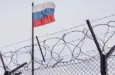 View of russian flag behind barbed wire against cloudy sky. Concept anti-Russian sanctions. A border post on the border of Russia.