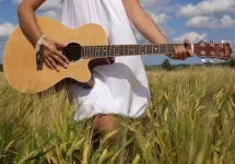 girl playing guitar in field over blue sky.