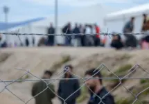 Barbed wire in refugee camp. Migrants behind chain link fence in camp. Group of people behind fence. Concept of prison^ freedom^ barrier^ security and migration. Refugees on their way to EU.