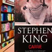 Paperback cover of Carrie by Stephen King shown on a bookshop shelf background