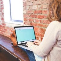 Woman accessing internet on laptop near brick wall