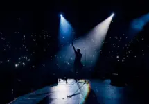 View from the stage stadium. Vocalist of a popular pop band on the background of the flashlights of phones during a concert. Fans switch on lights on smart phones on tribunes. Crowd waving cellphones