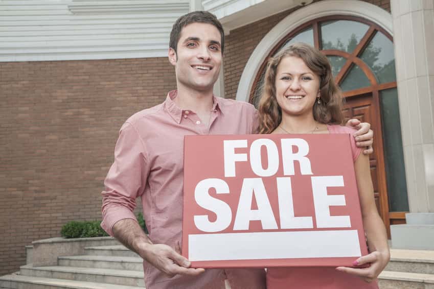 smiling-young-couple-holding-a-for-sale-sign