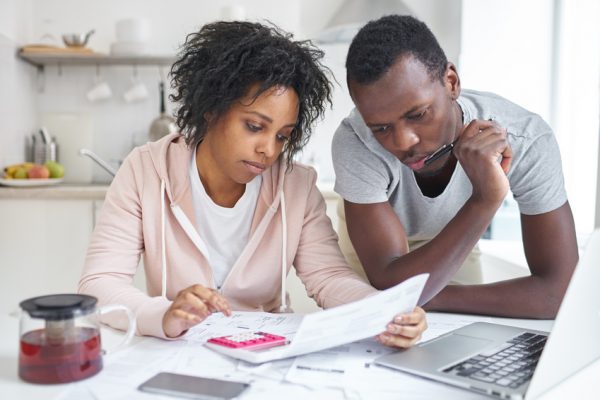 young-african-american-couple-doing-paperwork-together-planning-family-budget-calculating-domestic-expenses-sitting-at-kitchen-table-with-laptop-and-calculator-at-home-financial-problems-concept
