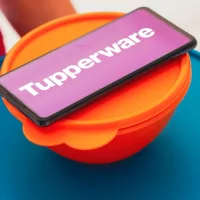 In this photo illustration^ a person carries various plastic products (containers) and a smartphone shows the Tupperware logo