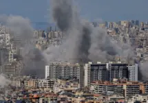 Multiple large plumes of thick grey smoke billow from residential apartment complexes following an explosion or missile strike in a crowded urban skyline. Jan 3 2021 in Iran