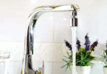 Open kitchen sink faucet flowing stream of water purified by domestic reverse osmosis with filters around. Front view. Horizontal composition.