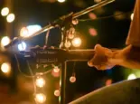 Rear view of the man sitting play acoustic guitar on the outdoor concert with a microphone stand in the front^ musical concept.