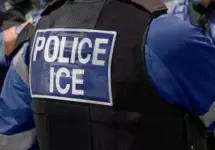 ICE police agent - Officer of Immigration and Customs Enforcement. Close-up of POLICE ICE marking on the back of a stab proof vest uniform worn by a trio of police officers at the scene of an incident